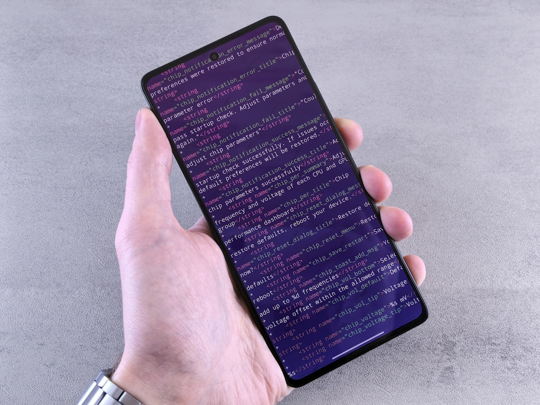 hand-holding-smartphone-displaying-lines-of-code-cmodnbbxfxc